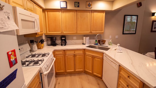 Una cocina con gabinetes de madera, una encimera blanca, una estufa y un microondas.