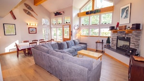 Amplia sala de estar con sofá modular, mesa de comedor, sillas y chimenea.