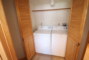Un cuarto de lavado con dos lavadoras blancas, puertas de madera y una lámpara sobre ellas.