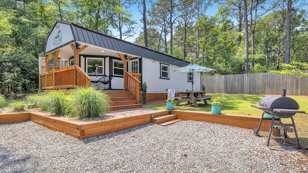 A house with a porch, a deck, a barbecue grill, and a wooden fence.