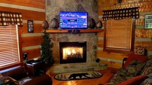 Ein gemütliches Wohnzimmer mit Kamin aus Stein, einem darüber montierten Fernseher und einem Teppich mit Bärenmotiv.