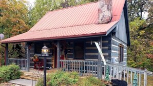 Eine rustikale Holzhütte mit rotem Metalldach, einem Steinkamin und einer Veranda mit Geländer.