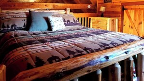 Ein Schlafzimmer einer Holzhütte mit einem Bett, ausgestattet mit gemusterten Betttextilien, einem Holz-Kopfteil und einer rustikalen Atmosphäre.