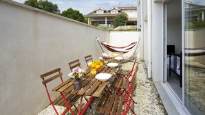 Un espace extérieur aménagé pour les repas, avec une table dressée pour quatre personnes, entourée de chaises. Un hamac est suspendu entre deux poteaux.