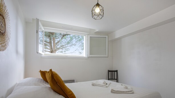 Une chambre à coucher avec un lit, une fenêtre, un miroir et un luminaire suspendu.
