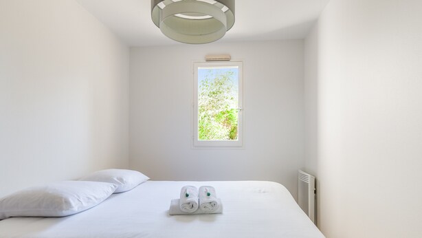 A bedroom with a bed, pillows, a window, and a radiator. - Appartement Charly - Welkeys (Cabourg)