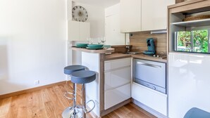 A modern kitchen with white cabinets, a wooden countertop, a sink, a coffee machine, and two bar stools. - Appartement Charly - Welkeys (Cabourg)