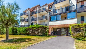 A multi-story residential building with balconies, a paved driveway, and a well-maintained lawn. - Appartement Charly - Welkeys (Cabourg)