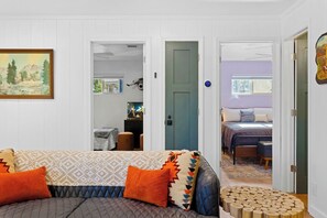 A room with a sofa, a TV, a door leading to another room, and a painting on the wall.