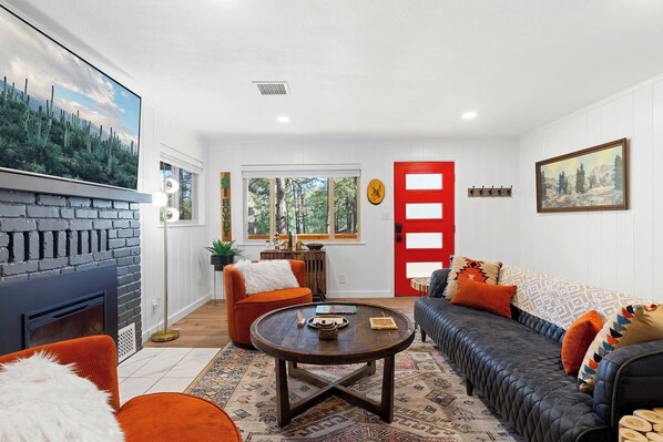 A living room with a fireplace, a sofa, a coffee table, and a red door.