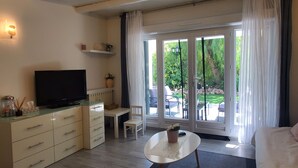 A hotel room with a TV, a small desk, a chair, a bed, and a view of the garden through the glass door. - MAGNIFICENT T2 58m2 air-conditioned PORT FREJUS 4/5 P in residential area, terrace, quiet and close to everything (Fréjus)