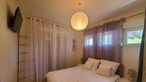 A bedroom with a bed, curtains, a bedside lamp, a wall-mounted TV, and a window with a view. - MAGNIFICENT T2 58m2 air-conditioned PORT FREJUS 4/5 P in residential area, terrace, quiet and close to everything (Fréjus)