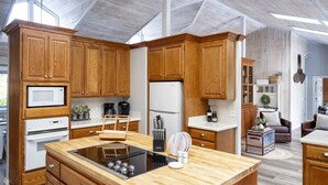 A modern kitchen with wooden cabinetry, a central island, and a built-in stove. - A luxurious vacation rental just minutes away from the beach! (Fort Bragg)
