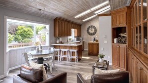 A spacious kitchen with wooden cabinets, a large clock, and a dining area with a round table and chairs. - A luxurious vacation rental just minutes away from the beach! (Fort Bragg)