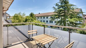 Un balcon doté d’une barrière en verre, d’une table en bois et d’un banc.