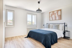 Un dormitorio con una cama, dos mesitas de noche, un radiador y una ventana.