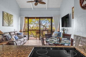 Une cuisine équipée d’une cuisinière, un coin repas avec une table et des chaises, un canapé et un balcon avec vue sur les arbres.