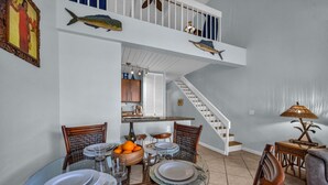 A dining area with a table set for four, a staircase, and a kitchen in the background. - Bright and Cheery Maui Vista 2 BR/2BA   MV2420 (Kihei)