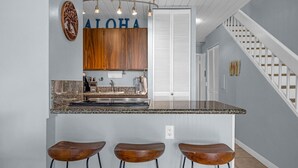 A kitchen with a granite countertop, wooden cabinets, and a bar stool area. - Bright and Cheery Maui Vista 2 BR/2BA   MV2420 (Kihei)