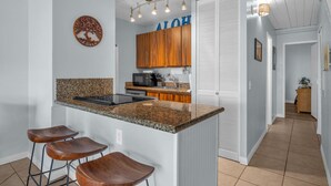 A kitchen with a granite countertop, wooden cabinets, a built-in microwave, and a bar stool area. - Bright and Cheery Maui Vista 2 BR/2BA   MV2420 (Kihei)