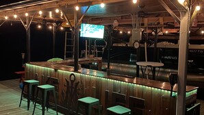 Ein Außenbereich mit Bar, Holzdeck, Barhocker und Lichterketten.