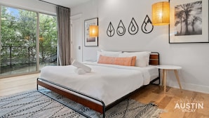Un dormitorio moderno con una cama grande, una mesita de noche pequeña y vistas a árboles a través de un ventanal corredero.