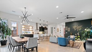 Una cocina moderna con armarios blancos, un comedor con mesa y sillas de madera, y una sala de estar con sofá azul y una pared de acento negra.