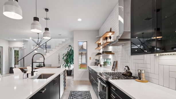 Una cocina moderna con una isla central, armarios blancos y negros, e iluminación colgante.