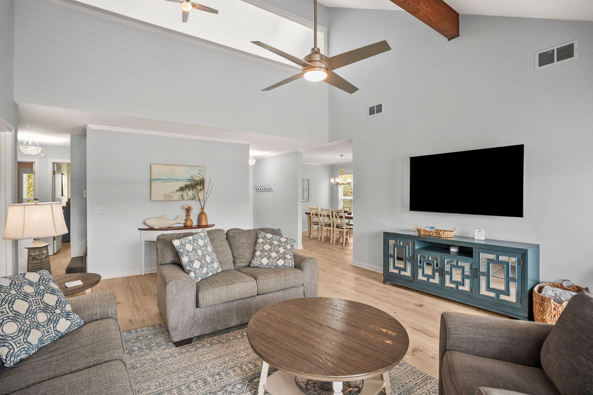A spacious living room with a grey sofa set, a round coffee table, and a flat-screen TV mounted on the wall.