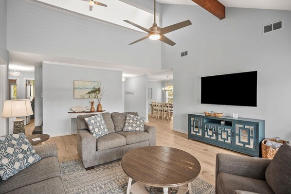 A spacious living room with a grey sofa set, a round coffee table, and a flat-screen TV mounted on the wall.