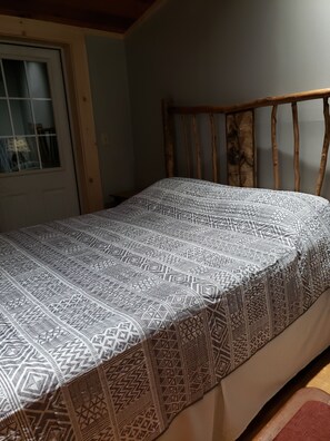 Un lit avec une couvre-lit à motifs, une tête de lit en bois et une fenêtre avec des stores.