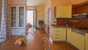 A compact kitchen with yellow cabinets, a dining table with fruit, and a TV in the background. - Nanà - Sweet Dreams in Florence (Firenze)