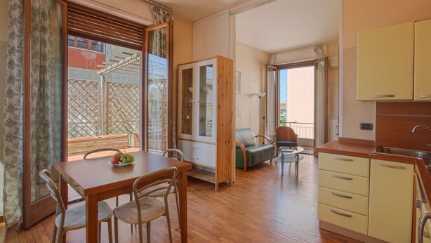 A room with a wooden dining table, chairs, a sofa, a small kitchen area, and a sliding glass door leading to a balcony. - Nanà - Sweet Dreams in Florence (Firenze)