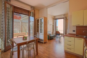 A room with a wooden dining table, chairs, a sofa, a small kitchen area, and a sliding glass door leading to a balcony. - Nanà - Sweet Dreams in Florence (Firenze)