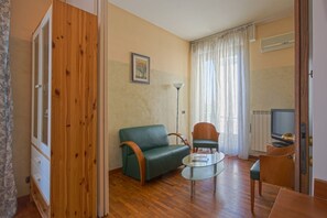 A compact living space with a wooden wardrobe, a green sofa, a small table, a chair, and a television.