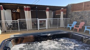Ein Whirlpool mit sprudelndem Wasser, umgeben von einer Holzterrasse und einem weißen Zaun.