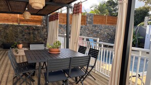 Eine Terrasse im Freien mit einem Holztisch und Stühlen, einem Topfpflanzen und Blick auf den Ozean.