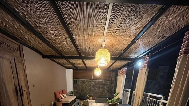 Eine Holzterrasse mit Esstisch und Stühlen, einer hängenden Leuchte und einer Steinwand.