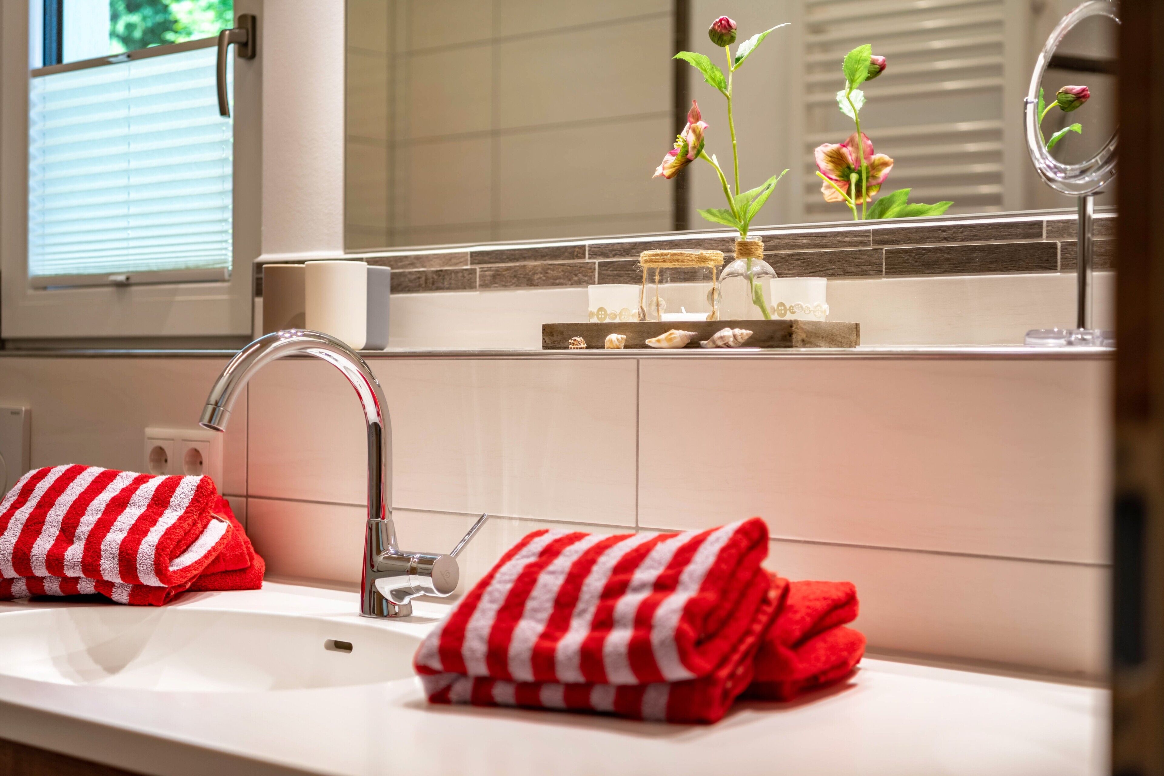 A bathroom with a sink, two red and white striped towels, a mirror, and a vase with flowers.