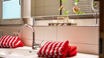 A bathroom with a sink, two red and white striped towels, a mirror, and a vase with flowers.
