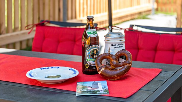 Une table avec une bouteille de bière, un pot de sauce, un bretzel et une assiette sur laquelle se trouve une carte postale.