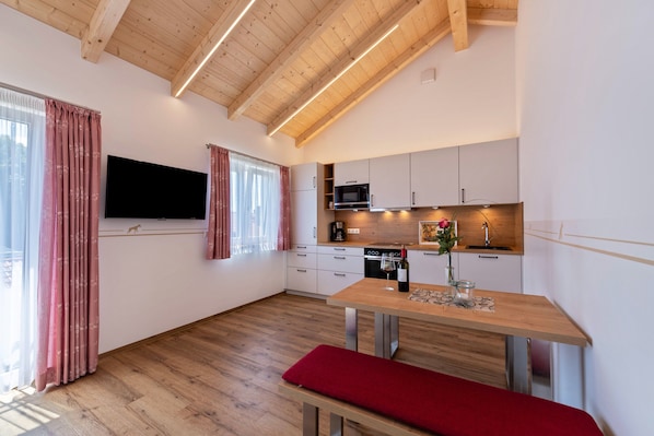 A modern kitchen with a wooden ceiling, a flat-screen TV, and a dining area with a bench. - Holiday Apartment Ronja with Open Terrace & Wi-Fi (Unknown)