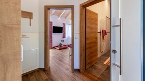 Un couloir doté d’un plancher en bois, d’une porte blanche et d’une vue sur une pièce où se trouvent un téléviseur et un panier pour animal de compagnie.