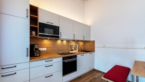 Une cuisine moderne avec des meubles blancs, un plan de travail en bois, un four à micro-ondes encastré, une machine à café et un petit tabouret rouge.