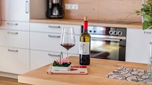 Une cuisine avec des meubles blancs, une machine à café et une bouteille de vin posée sur un plan de travail en bois.
