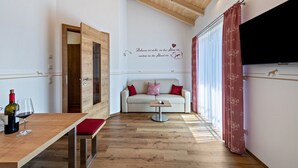 Une pièce avec un plafond en bois, un canapé avec des coussins rouges, une petite table avec une bouteille et un verre, et un mur orné d’une citation décorative.