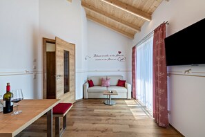 A room with a wooden ceiling, a sofa with red cushions, a small table with a bottle and glass, and a wall with a decorative quote.