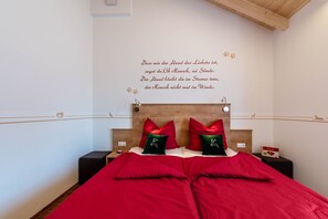 A bedroom with a wooden headboard, red bedding, and a wall with a German quote. - Holiday Apartment Ronja with Open Terrace & Wi-Fi (Unknown)