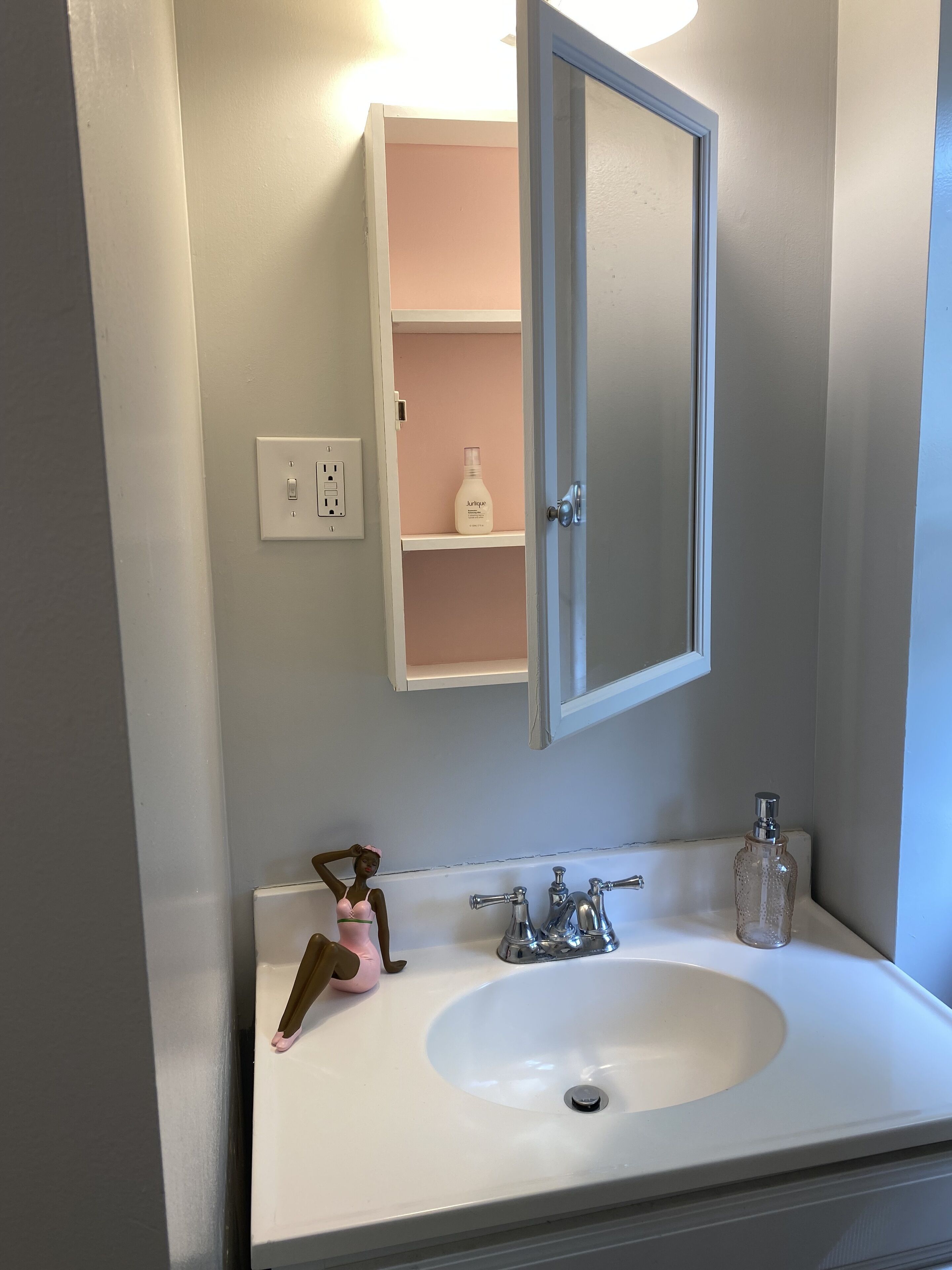 A bathroom with a white sink, a mirror, and a pink shelf with a bottle.