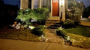 Una casa a due piani con una porta rossa, un piccolo portico e un giardino anteriore ben illuminato.